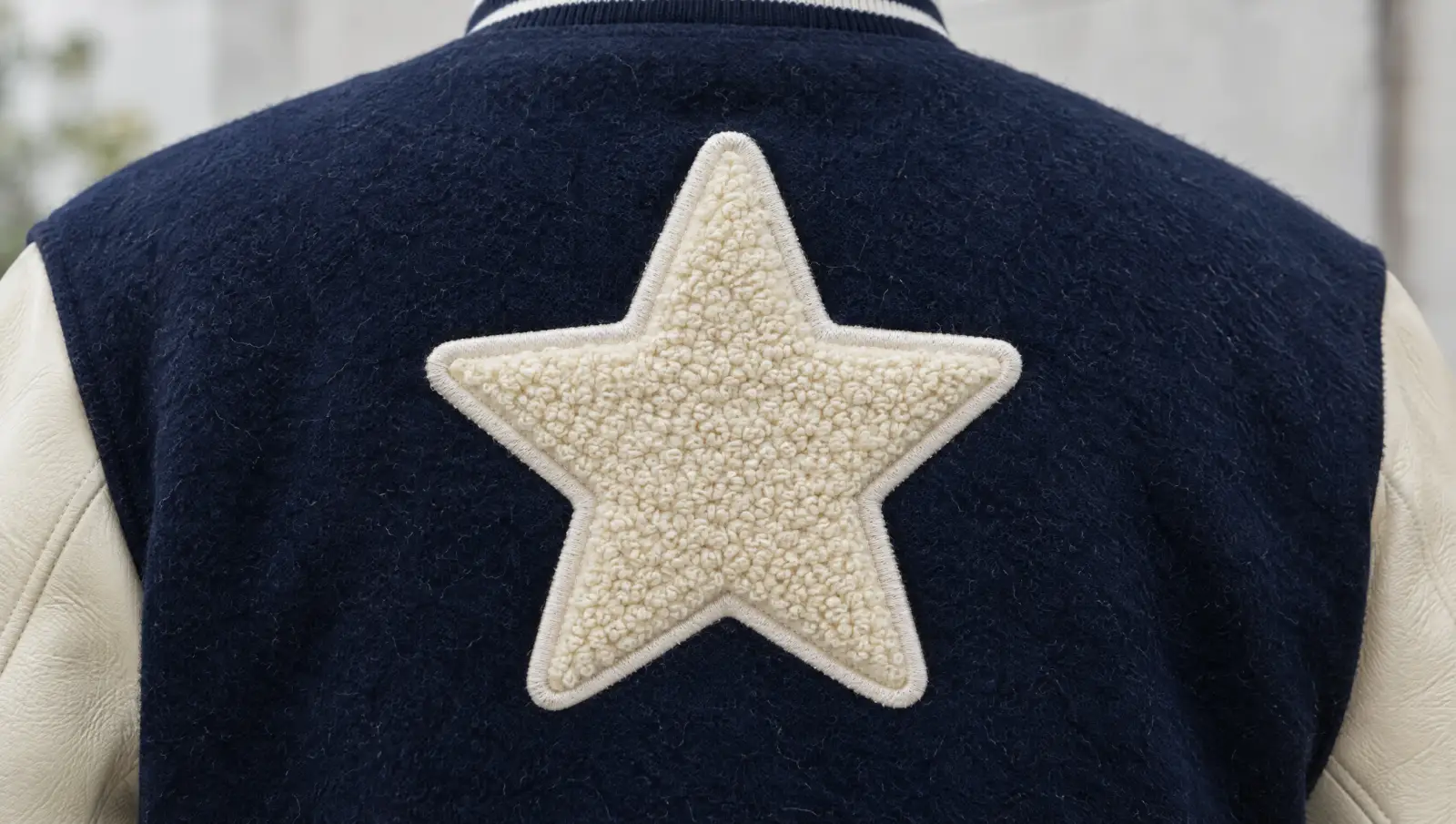 A cream chenille star patch with a satin-stitched border on the back of a navy varsity jacket