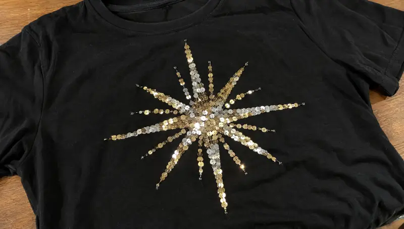 A black T-shirt with a starburst of silver and gold sequins
